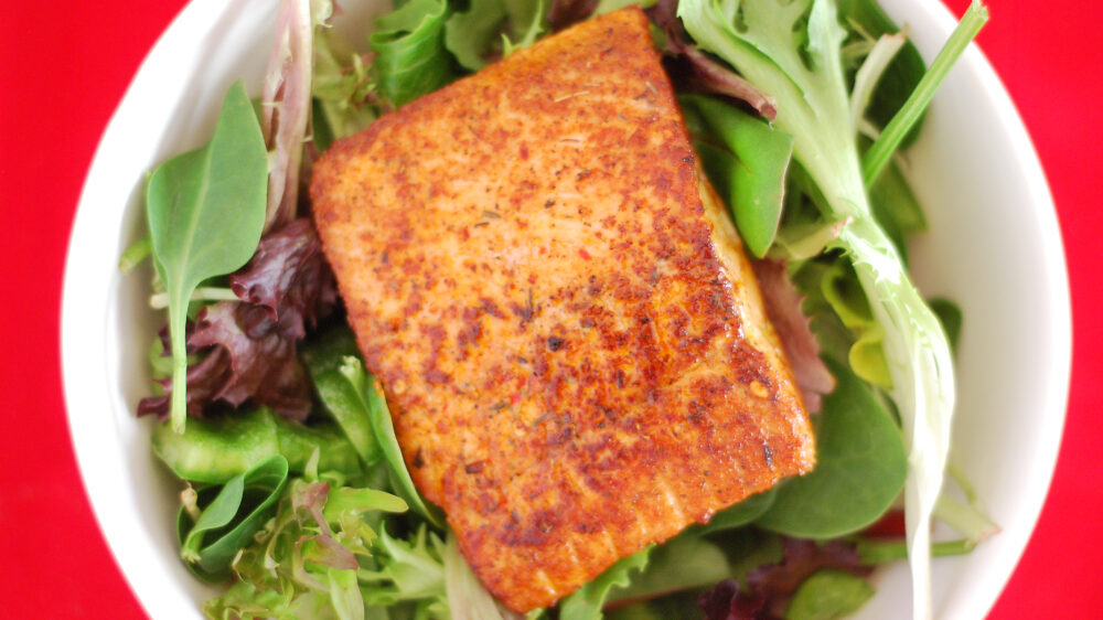 a piece of blackened salmon on a bed of greens
