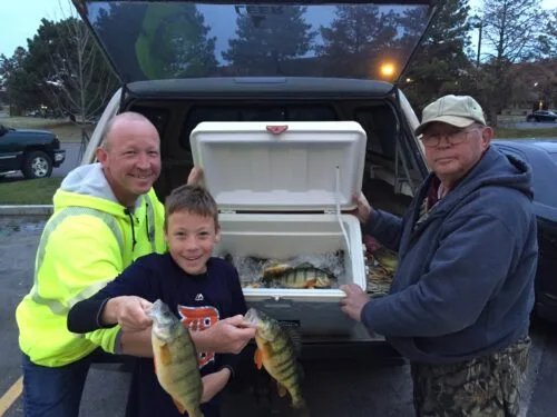 two men and boy with a cooler of yellow perch