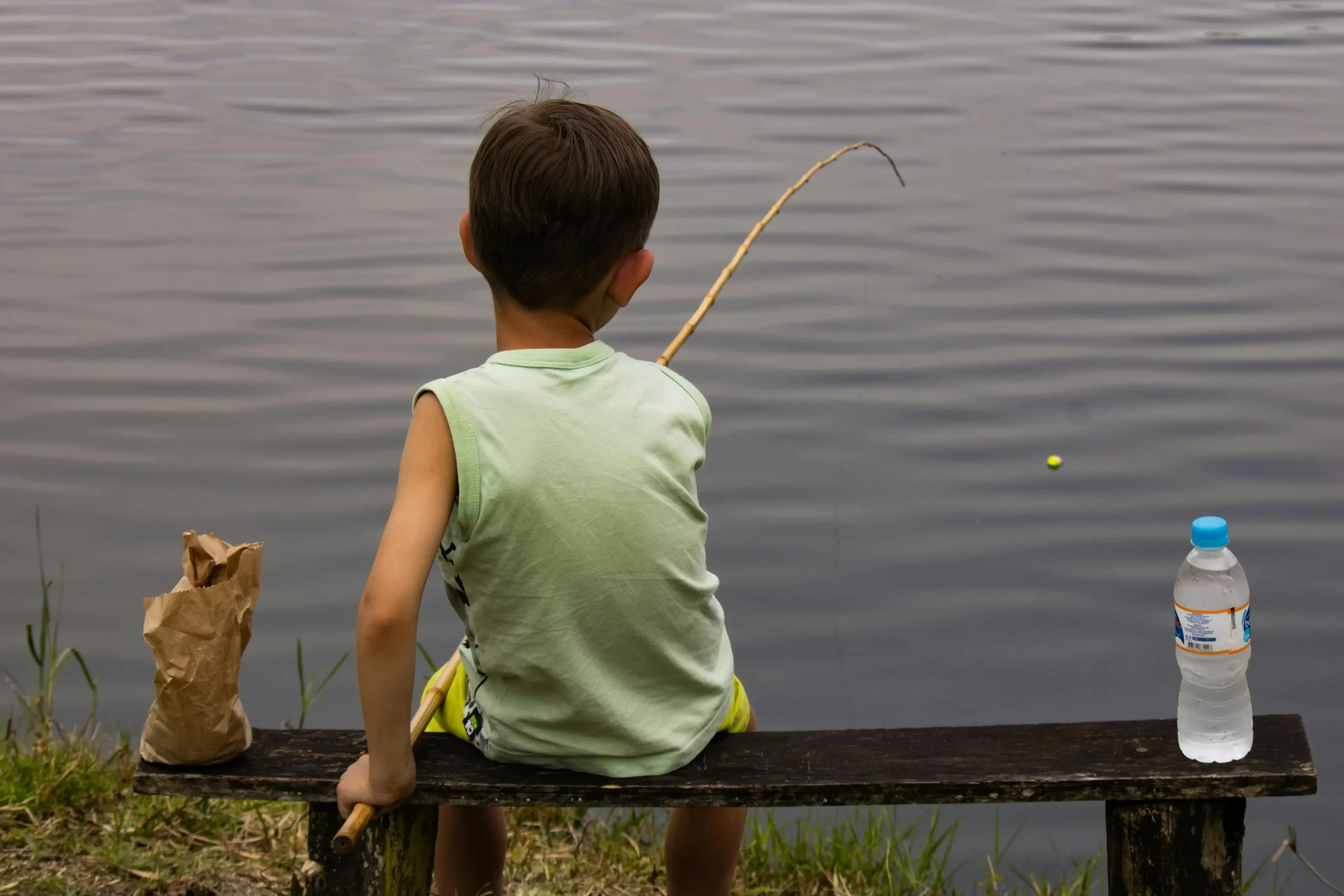 child fishing from a bench on the lake